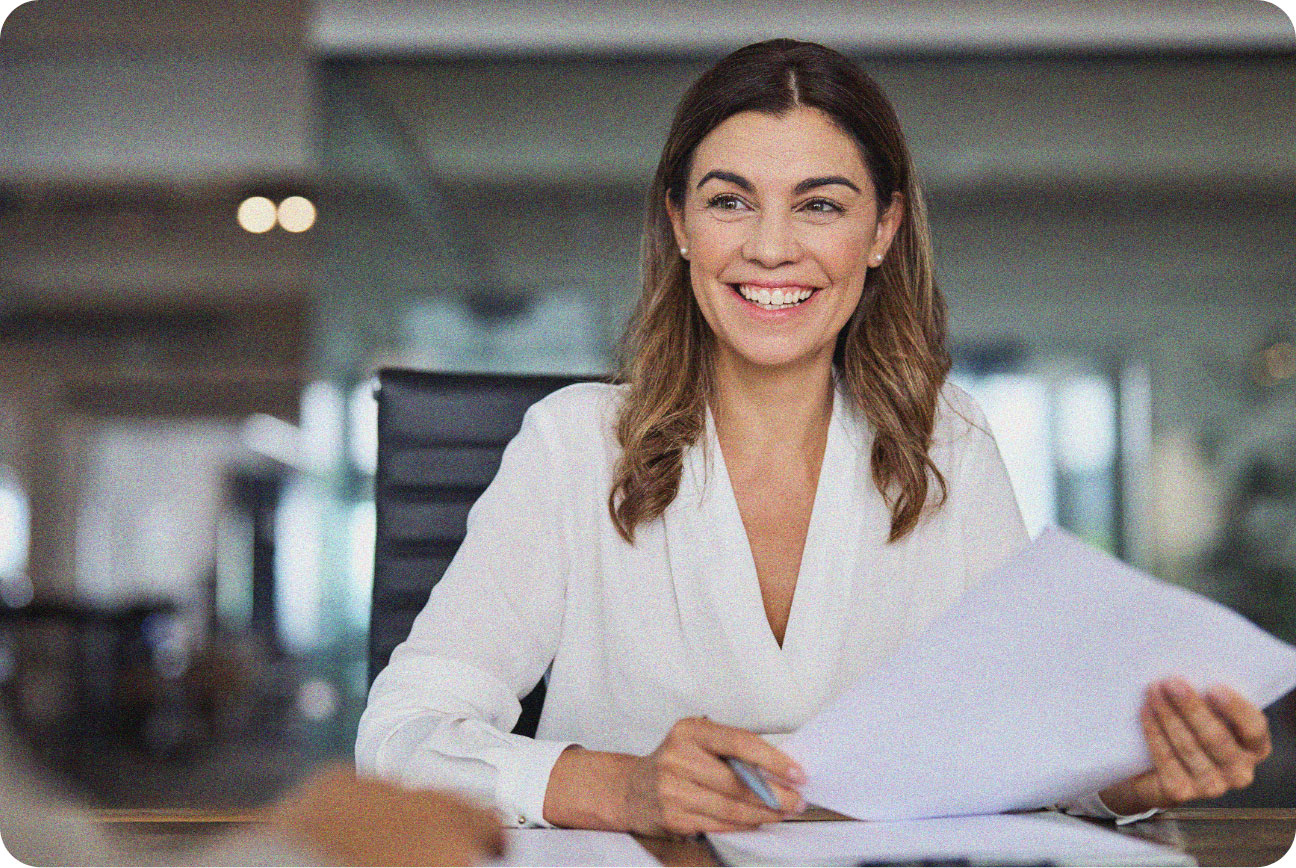 Woman smiling to somebody off camera while holding a sheet of white paper